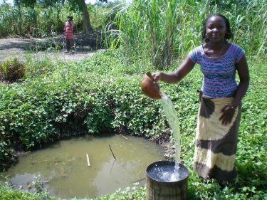 Een vrouw giet schoon water in een emmer in Malawi.
