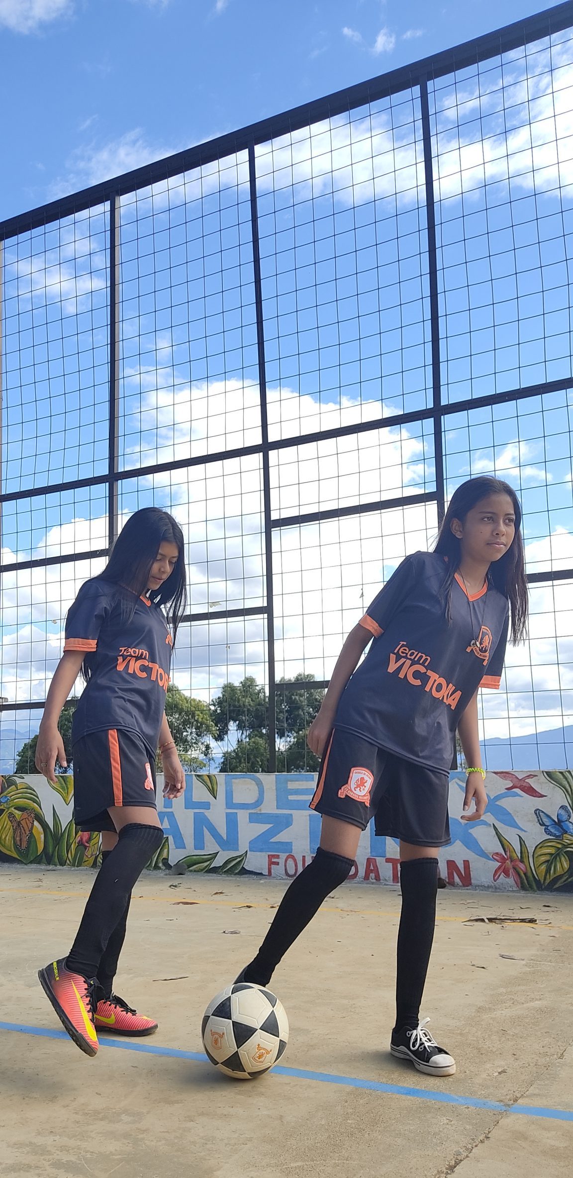 2 meisjes met voetbalshirts en bal op een straatvoetbalveldje in Colombia.