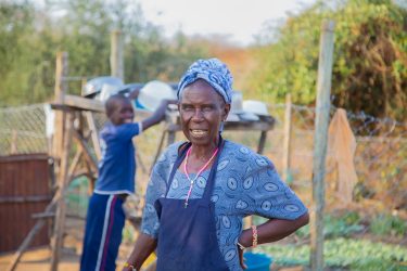 Een vrouw staat bij een moestuin met een jonge jongen op de achtergrond.