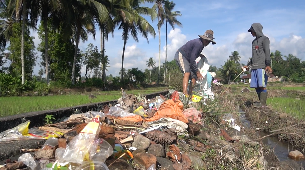 Twee mensen staan in een rivier gevuld met plastic afval.