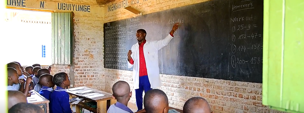 Een man staat voor een schoolbord en een groep kinderen kijkt toe.